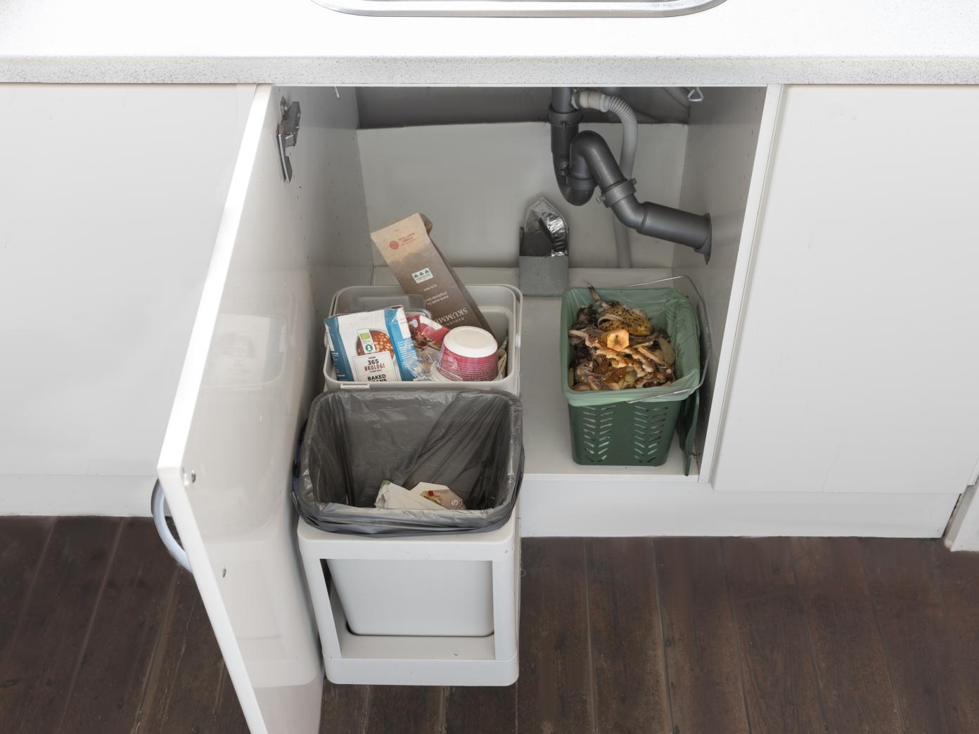 En køkkenlåge med udtrækssystem med to affaldsspande til plast og restaffald. Ved siden af på bunden i skabet står kurven til madaffald, så denne også er lettilgængelig.