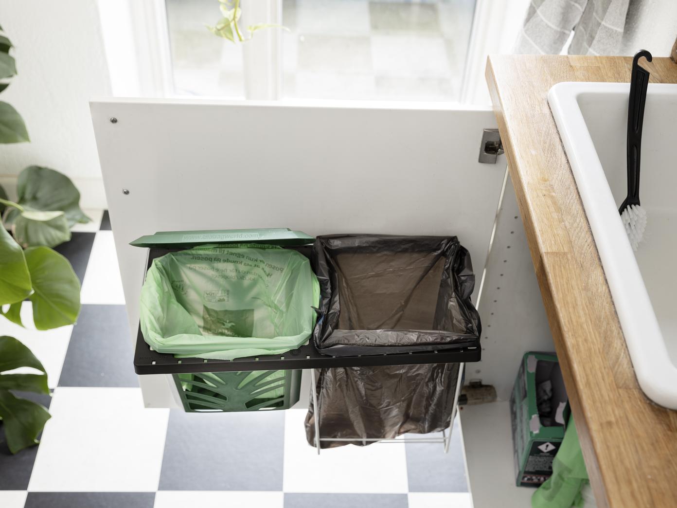 På en køkkenlåge under vasken er fastgjort et traditionelt skraldestativ i metal. På skraldestativet er monteret en holder, som køkkenkurven kan sidde i. Skraldestativet kan nu have både affaldspose og den grønne kurv til madaffald.